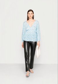 Blusa floral azul claro com decote em V profundo, combinada com calças de couro pretas. A modelo segura uma bolsa branca e usa sandálias azuis claras.
