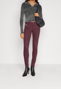 Jeans skinny burdeos y una camiseta de manga larga ajustada gris con escote redondo. El conjunto incluye botas negras de tacón puntiagudas y un pequeño bolso negro.