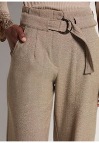 Beige hoge taille broeken met een stofstructuur, voorzien van een grote zwarte ronde gesp en zijzakken, benadrukt met plooien.