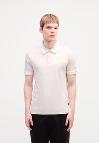 Polo shirt bej deschis din bumbac, cu guler clasic, mâneci scurte cu accente albe și un logo subtil pe piept.