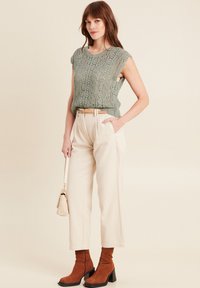 Maglione leggero verde chiaro con maniche a scallop, pantaloni beige a gamba larga, stivaletti marroni con tacco e una piccola borsa beige.