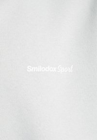 Biała sportowa tkanina z teksturowanym wzorem dzianiny; zawiera nazwę marki "Smilodox Sport" w pogrubionym, wypukłym druku.