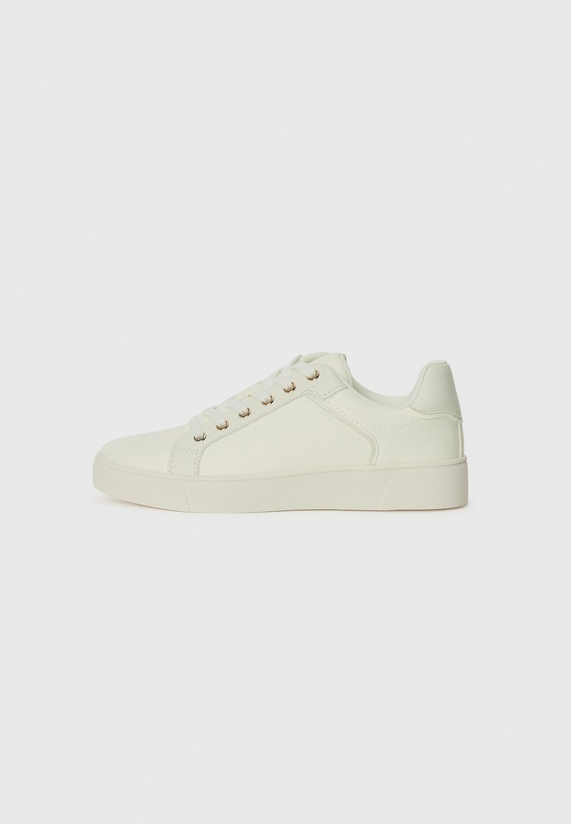 White synthetic sneakers with a smooth texture, rounded toe, and flat rubber sole. Features six eyelets and gold-toned hardware accents.
