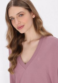 Maglione a maniche lunghe con scollatura a V in morbido tessuto lavanda, caratterizzato da una trama a maglia e una discreta logo di ancora vicino al colletto.