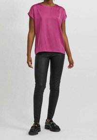 Top fucsia a maniche corte in un tessuto morbido, abbinato a pantaloni neri slim-fit e scarpe con plateau nere con una fascia decorativa.