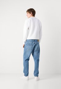 Hvid sweatshirt med lange ærmer, parret med lysblå, løstsiddende denimjeans. Fodtøjet er hvide sneakers, synlige for neden.