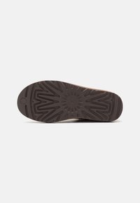 Suela de zapato de goma marrón con un patrón en zigzag y acentos circulares. Presenta una superficie texturizada para mayor tracción. Diseño de puntera redondeada.