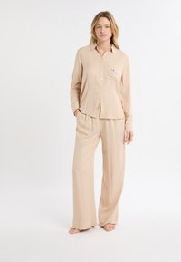 Beżowy, pasiasty zestaw piżamowy składający się z koszuli z długim rękawem i kieszonką oraz luźnych spodni. Miękka tkanina z zapięciem na guziki.