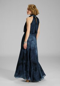 Maxime dress in dark navy chiffon with a floral pattern, halterneck and open back details. Flowing silhouette with a layered design.