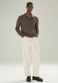 Braun langärmliges Polohemd mit zwei Knöpfen, cremefarbene weite Hose und schwarze Schnürschuhe. Glatte Textur durchgehend.