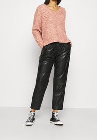 Rosa stickad tröja med V-ringning och sidoklipp, matchad med svarta läderbyxor och svarta högskurna sneakers.