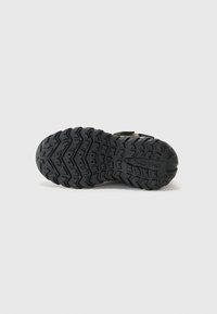 Semelle en caoutchouc noir avec un motif de bande de roulement en zigzag, mettant en avant des accents en relief et le logo de la marque. Conception robuste pour une traction et une durabilité.