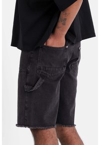 Shorts in denim nero con orlo sfrangiato, dotati di tasche laterali e passanti per cintura. Tessuto testurizzato con una finitura leggermente sbiadita.