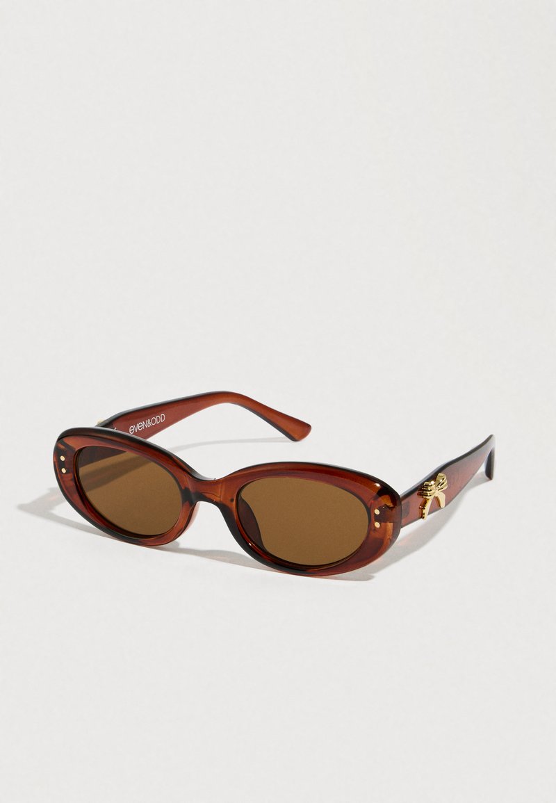 Lunettes de soleil écaille de tortue brunes avec des verres ovales, une monture dorée accentuée sur le côté, et une texture plastique lisse.