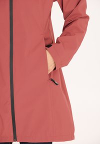 Vandafvisende pink jakke med lange ærmer, lynlås foran og sidelommer. Har en glat overflade og sorte detaljer.