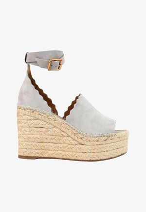 Sandale compensée en daim gris clair avec bords festonnés, semelle plateforme en jute tressée et bride à la cheville avec boucle dorée.