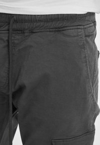 Tamne sive cargo hlače s elastičnim pojasom, višestrukim džepovima i mekim, teksturiranim materijalom. Minimalni vidljivi detalji šavova.