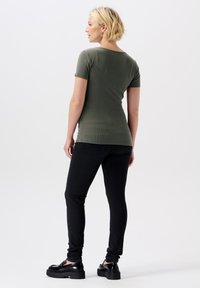 Un top à manches courtes côtelé vert olive associé à un jean noir slim. Modèle vu de dos, portant des chaussures à plateforme noires.