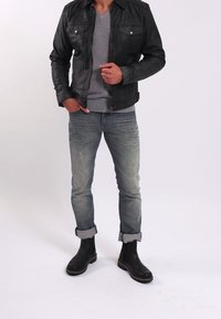 Černá kožená bunda, šedé tričko s V výstřihem, světle modré roztrhané džíny ohrnuté na kotnících, černé kozačky po lýtka s hnědými podrážkami.