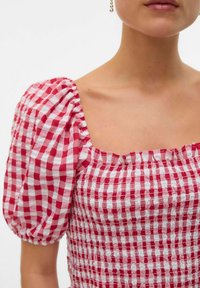 Top a maniche puff rosso e bianco a quadri con texture arricciata. Scollo quadrato, volant arricciati sulle maniche, tessuto leggero.