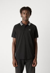 Camisa polo negra hecha de tela suave, con un cuello clásico con rayas blancas y un pequeño parche de logo en el pecho.