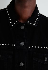 Black denim jacket featuring silver studs along the collar and front, with metal buttons and a sturdy, textured fabric.