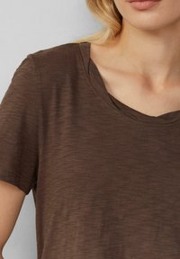 Braunes, kurzärmliges T-Shirt aus weichem, strukturiertem Stoff. Es hat einen Rundhalsausschnitt und eine lockere Passform mit subtilen Stoffvariationen.