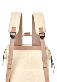 Mochila de color crema con material texturizado, correas ajustables en color marrón claro y herrajes negros. Cuenta con un cierre de cremallera y un bolsillo frontal.