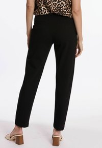 Pantalons noirs fuselés en tissu extensible, dotés de poches arrière et d'une finition lisse. Associés à des sandales beiges à talons blocs.