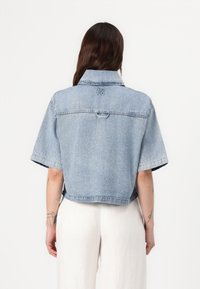 Giacca di jeans azzurro chiaro con maniche corte, design leggermente cropped e retro ricamato con il logo "HUGO". Texture liscia e stile casual.