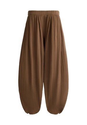 Femme portant un pantalon marron texturé ample, taille haute avec poches latérales et un haut court blanc sans manches.