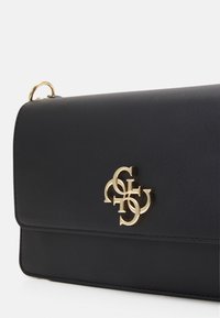 Czarna skórzana torebka z złotym akcentem logo. Charakteryzuje się gładką teksturą, wyraźnym kształtem oraz zapięciem na klapkę.