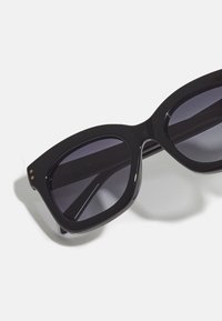 Black oversized sunglasses with dark tinted lenses. Made from shiny plastic, featuring gold accents and a geometric frame design.