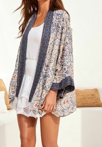Lekki kimono z kwiecistym wzorem w delikatnych kolorach, granatowymi wykończeniami, otwartym kroju z przodu oraz zwiewnymi rękawami, wykonany z oddychającego materiału.
