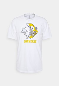Camiseta blanca con un gráfico de un esqueleto sosteniendo una estrella dentro de un logotipo de chevron amarillo de Converse y el texto "CONVERSE" en amarillo debajo.