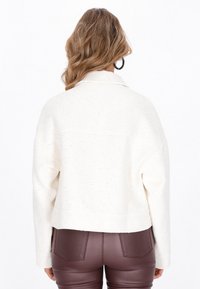 Witte gestructureerde jas met een kraag, met een cropped ontwerp. Gemaakt in combinatie met aansluitende bordeauxrode broek. Geen zichtbare patronen of hardwaredetails.