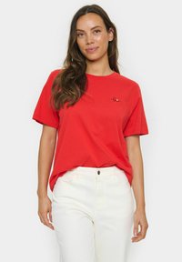 Red short-sleeve t-shirt made of cotton, featuring a small black embroidered "love" text on the left chest area. Paired with white pants.