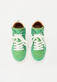 Groene hoge sneakers met perforatietextuur, witte veters, tan interieurvoering en een treklip aan de hiel.
