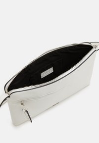 Pochette en cuir texturé blanc avec fermeture éclair, doublure intérieure noire et une petite poche. Dotée d'une fermeture éclair et d'un bord en argent.