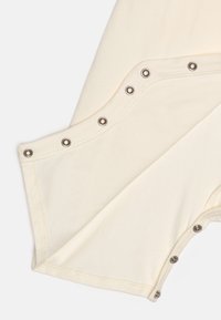 Akré színű szövet sima felülettel, ezüst színű patent gombokkal az él mentén, tiszta, minimalista designt teremtve.