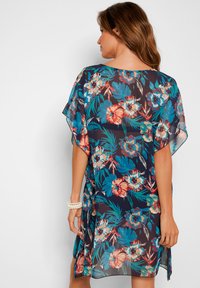 Kimono floreale in tessuto trasparente blu navy, caratterizzato da vivaci motivi rossi, blu e verdi. Fit ampio con fianchi spaccati e maniche a pipistrello.