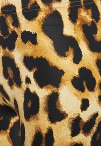 Løveprint leggings med en kombination af sort, brun og tan farver, lavet af et struktureret stof med synlige sømme ved taljen.
