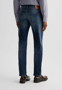 Jeans in denim blu scuro con una vestibilità slim, dotati di un'etichetta in pelle sulla vita posteriore e due tasche posteriori. Abbinati a scarpe marroni lucide.