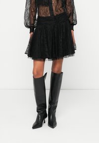 Černá krajková mini sukně s vícetrojným designem a nařaseným pasem, doplněná černými koženými botami na vysokém podpatku s špičatou špičkou.