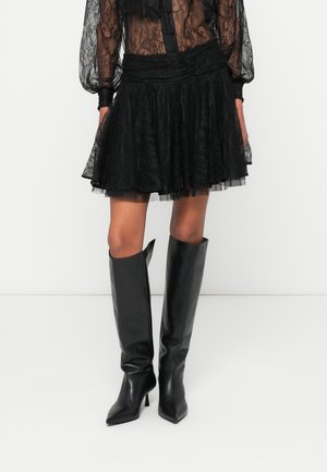 Zwarte kanten mini-rok met een gelaagde structuur en een geplooide tailleband, gecombineerd met zwart leren knielaarzen met een spitse neus.