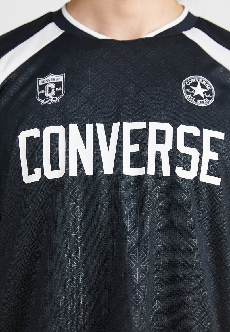 Jersey deportivo negro con gran texto blanco "CONVERSE", patrón geométrico, mangas cortas con acentos blancos y logotipos de la marca en el pecho.