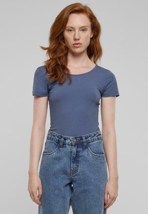 Blå kortermet bodysuit laget av glatt stoff, kombinert med høyden på faded blå denim jeans med synlige sømmer og knapppdeler.
