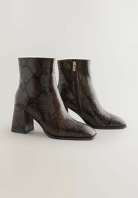 Kasta čūskas raksta potīšu zābaki ar kvadrātveida purngalu, augstu blokveida papēdi un sānu rāvējslēdzēju. Gluda tekstūra ar spīdīgu apdari.