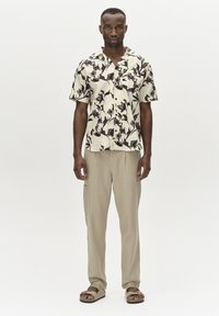 Chemise à manches courtes fleurie en crème avec des motifs violet foncé, associée à un pantalon beige clair et des sandales marron. Design simple et coupe décontractée.
