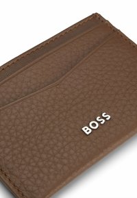 Portafoglio in pelle marrone con superficie texturizzata, cuciture visibili e logo "BOSS" argentato sulla parte anteriore. Tre scomparti per le carte.